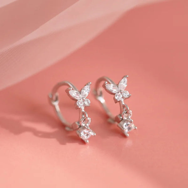 Pair of sterling silver butterfly zircon stud earrings displayed on a soft pink background.