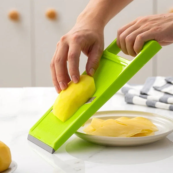 A hand is using a bright green handheld kitchen vegetable cutter to slice a piece of yellow squash on a white countertop.