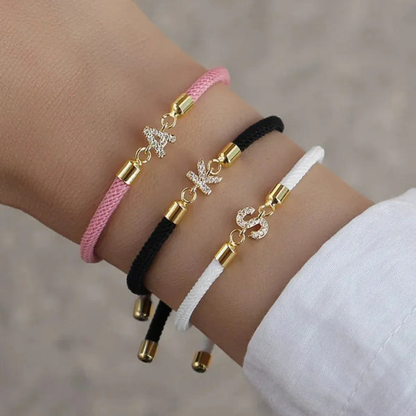 Handgelenk mit verstellbarem Buchstabenarmband aus rosa, schwarz und weißem Garn mit goldenen Akzenten.
