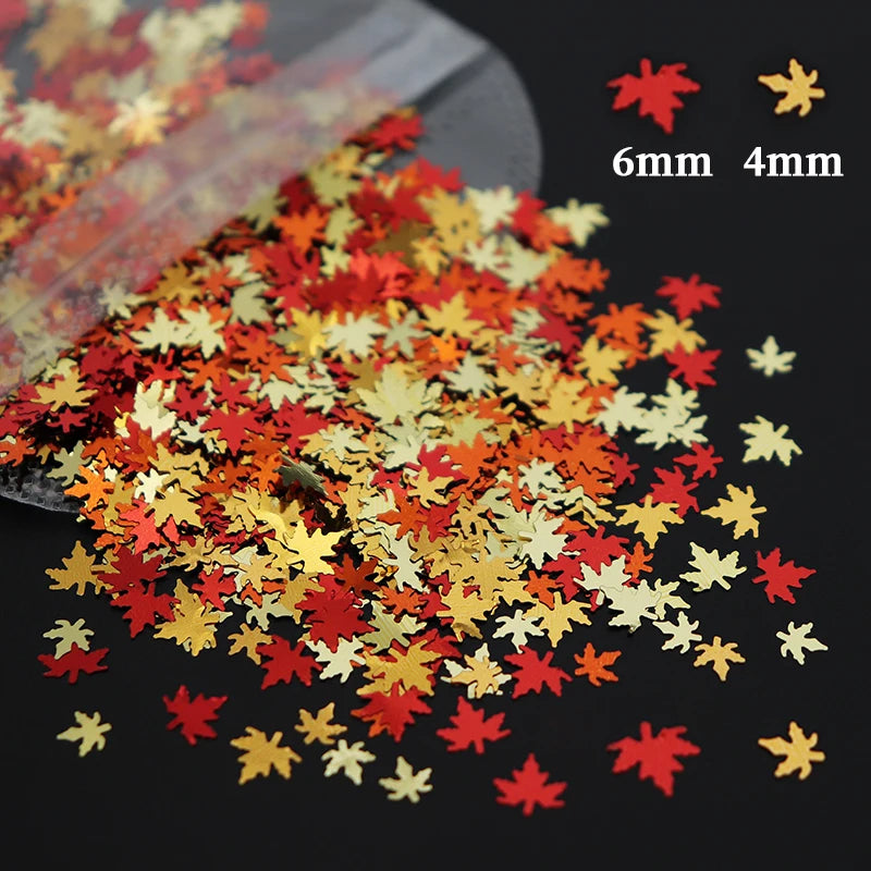 A scatter of shiny holographic star sequins in red, orange, and gold colors are displayed on a dark surface.