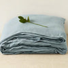 Light blue pure linen bed sheet set folded neatly with a green leaf on top