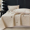 A beige floral quilted bedspread draped over a dark headboard in a bedroom setting.