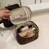 A brown faux suede cosmetic bag is open, revealing multiple pockets and a mesh lining with various makeup products inside.
