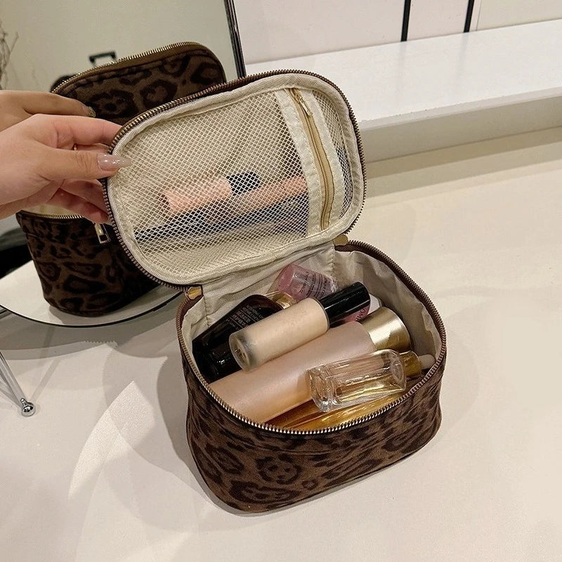 A brown faux suede cosmetic bag is open, revealing multiple pockets and a mesh lining with various makeup products inside.