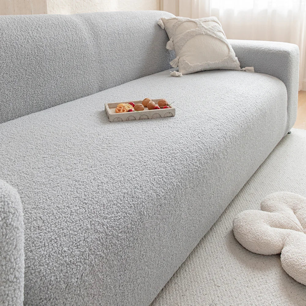 A light gray plush sofa cover with a decorative cushion and a small tray of food on the seat.
