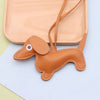 A tan PU leather dachshund puppy keychain with a stitched design is displayed on a light wooden tray.