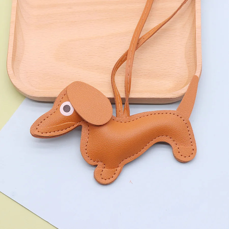 A tan PU leather dachshund puppy keychain with a stitched design is displayed on a light wooden tray.