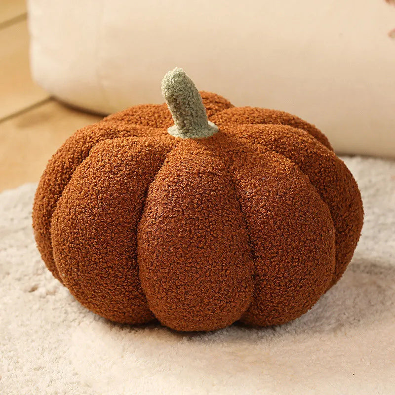 A round, textured brown pumpkin plush cushion with a green stem resting on a light surface.