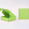 Eine limegrüne Wellpappkarton ist geöffnet und eine geschlossene Box daneben zu sehen.