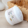 A white ball of cotton yarn labeled 100g resting in a woven bamboo basket.