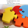 A hand is holding a yellow wooden puzzle piece next to red and blue puzzle pieces on a wooden surface.