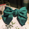 A dark emerald green silk bow hair clip with a satin finish displayed on white paper.