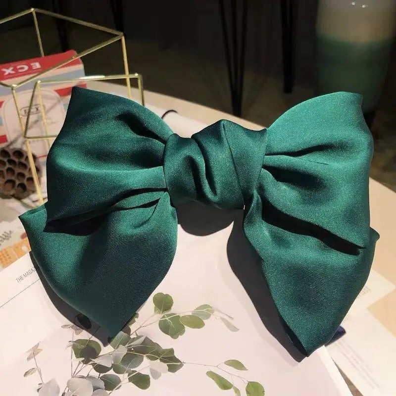 A dark emerald green silk bow hair clip with a satin finish displayed on white paper.