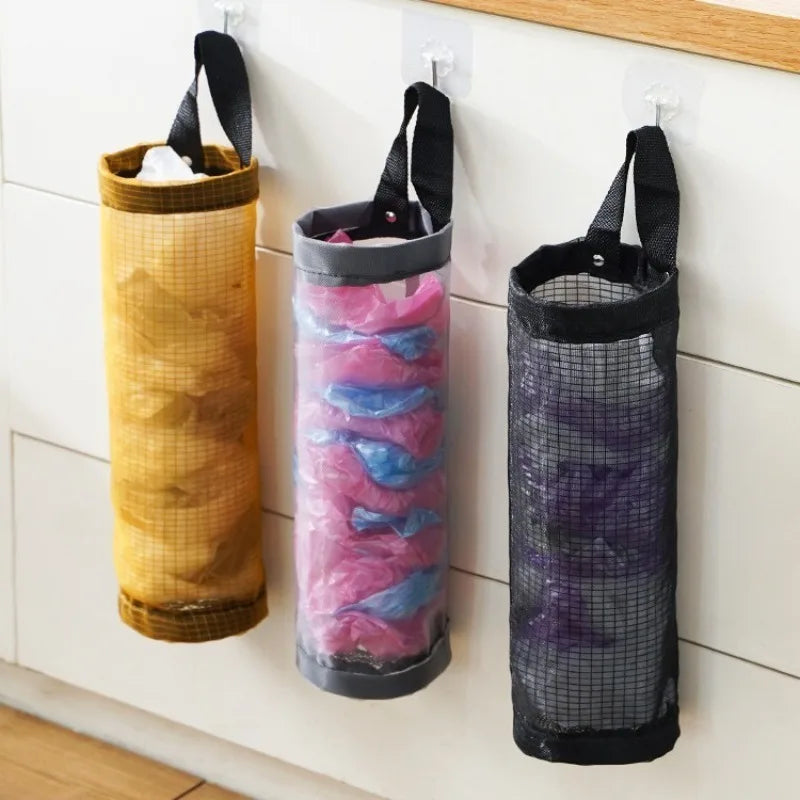 Wall-mounted mesh bag dispenser with three vertical bags in gold, pink, and purple colors