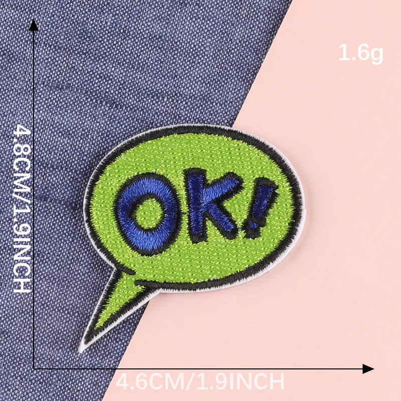 A bright lime green embroidered speech bubble patch with the text OK! on a dark blue fabric background.