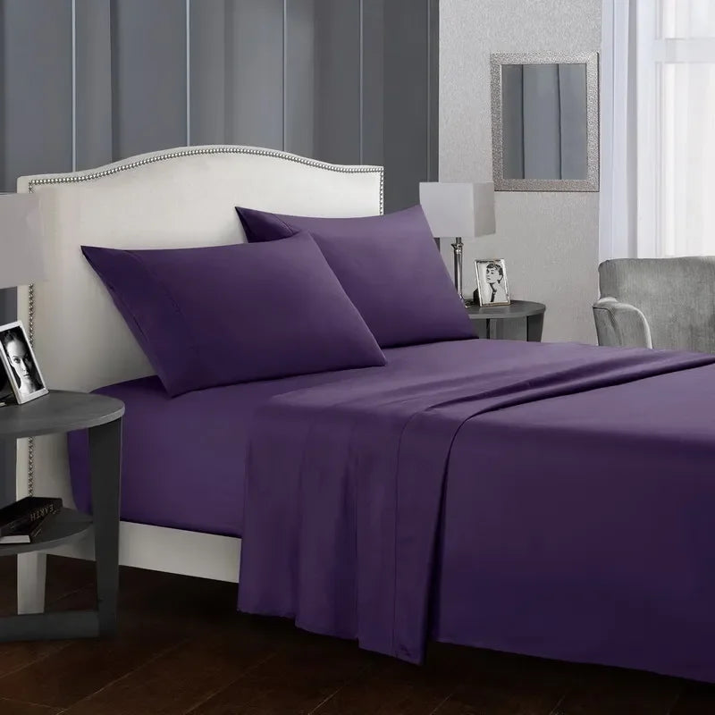 A purple bedding set with a fitted sheet, flat sheet, and pillowcases is displayed on a bed in a bedroom setting.