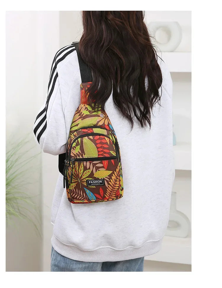A person is wearing a colorful leaf print sling crossbody bag with multiple pockets on a light gray sweatshirt.