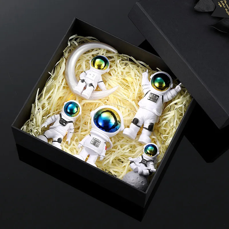 A set of five handcrafted astronaut figurine resin spaceman desk decor figures displayed in a black box with straw-like fille