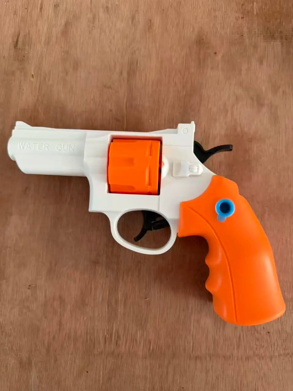 A white and orange mini mechanical revolver water gun is shown on a wooden surface.