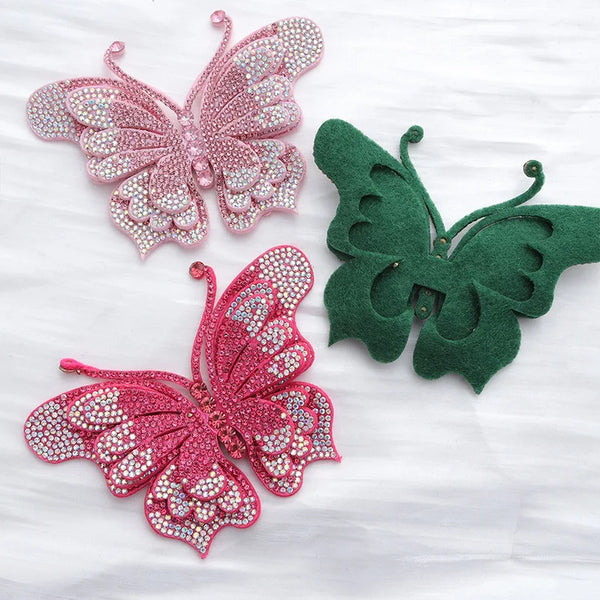 Two rhinestone butterfly appliqués, one pink and one green, displayed on white fabric.