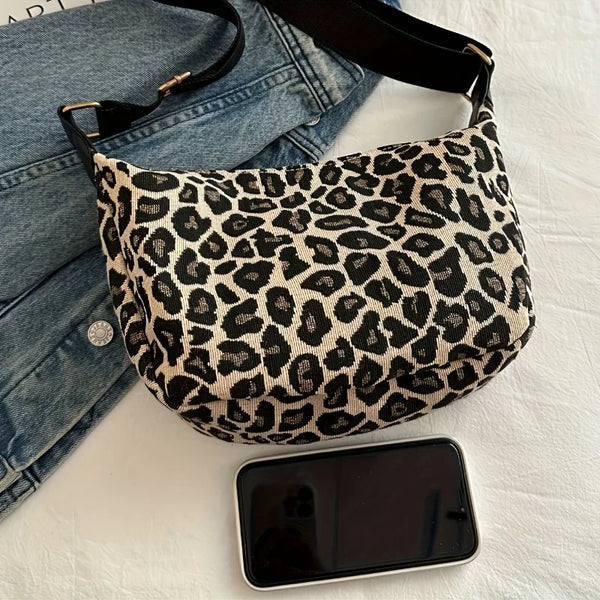 A black and tan leopard print nylon crossbody bag resting on a white surface next to a smartphone.