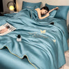 A teal ultra-soft comforter with gold embroidery and butterfly designs is draped on a bed, with a person resting on it.