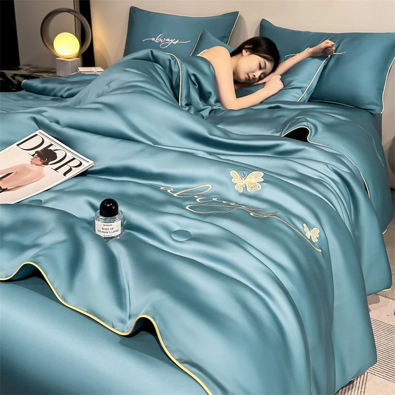 A teal ultra-soft comforter with gold embroidery and butterfly designs is draped on a bed, with a person resting on it.