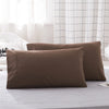 Two brown microfiber pillowcases resting on a light gray surface near a window with white grid curtains.