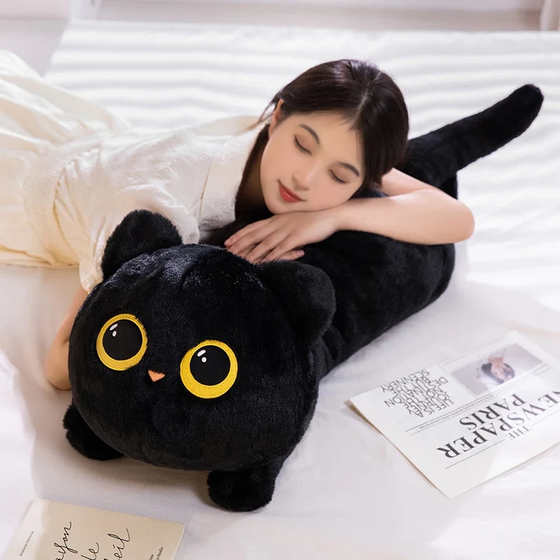A woman is relaxing and cuddling a soft black cat plush toy on a white surface.
