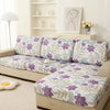 A floral elastic sofa cover in purple and green patterns protecting a beige upholstered sofa.