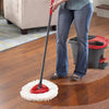 A person is using a red and black spin mop with a white microfiber pad on a wooden floor.