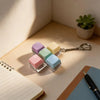 A collection of pastel colored mini mechanical keyboard fidget keychains resting on a wooden surface next to a notebook and a