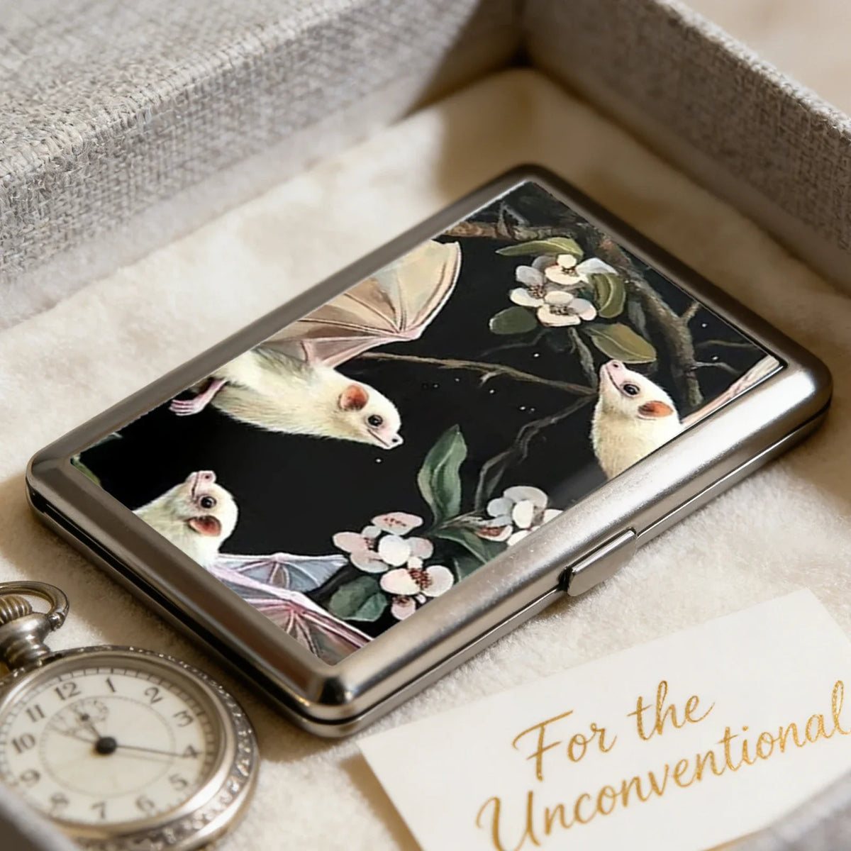 A vintage metal card and cash case with an art deco design featuring illustrations of bats and flowers.