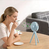 A woman is holding a white cup while sitting at a wooden table next to a blue flexible octopus USB fan on a tripod stand.