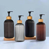 A set of two refillable soap dispensers with black glass bottles and wooden caps on a light blue surface.