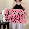 A woman models a pink and black leopard print plush jacquard throw blanket draped over her shoulder.