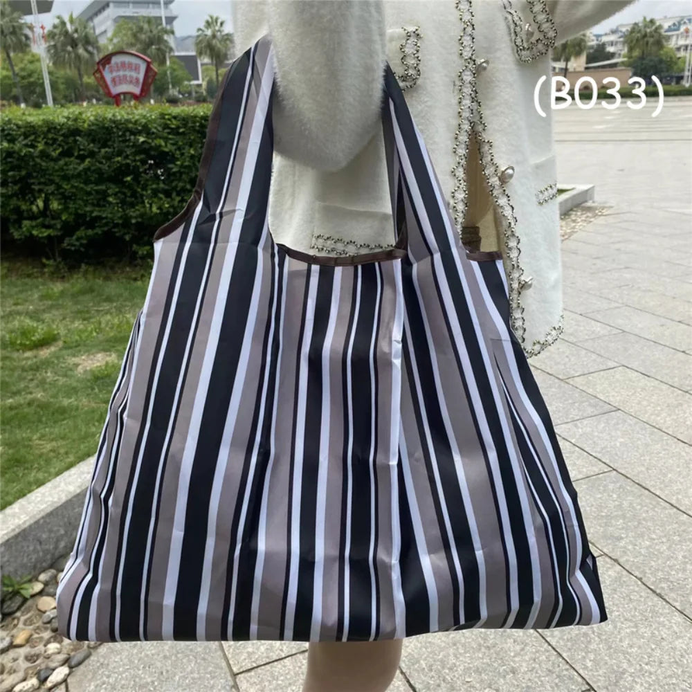 A black and white striped foldable oxford cloth tote bag carried by a person outdoors.