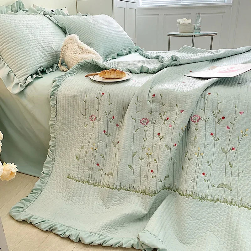 Light mint green quilted bedspread with embroidered floral patterns and ruffled edges