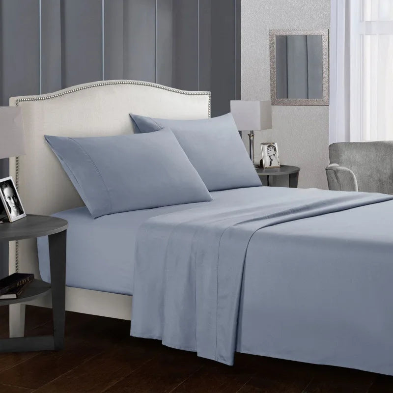 Un set de linge de lit en microfibre bleu clair présenté sur un lit avec une tête de lit rembourrée et une table de chevet.
