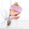 A person is using pink wrist washing bands to clean their face under running water.