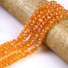 A strand of faceted orange crystal glass spacer beads is shown draped over a textured gold-colored cylindrical object.