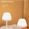 A white multi-function socket lamp with a shade sits on a wooden desk next to a pink charging base.