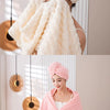 A woman is wrapped in a pink coral velvet bath towel and matching head wrap, looking content.