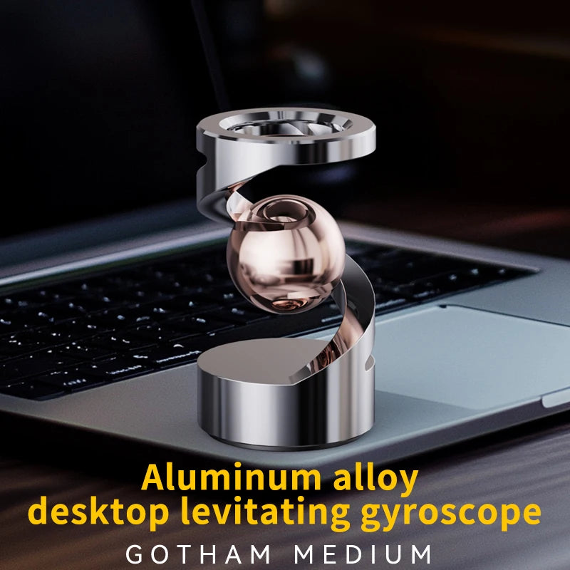 A silver aluminum alloy desktop levitating gyroscope spinning on a laptop surface.