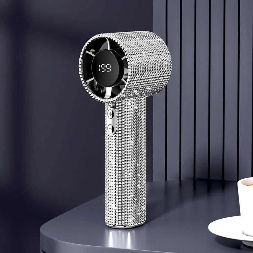 A silver sparkling diamond pattern portable fan with an LED display is shown on a dark surface.