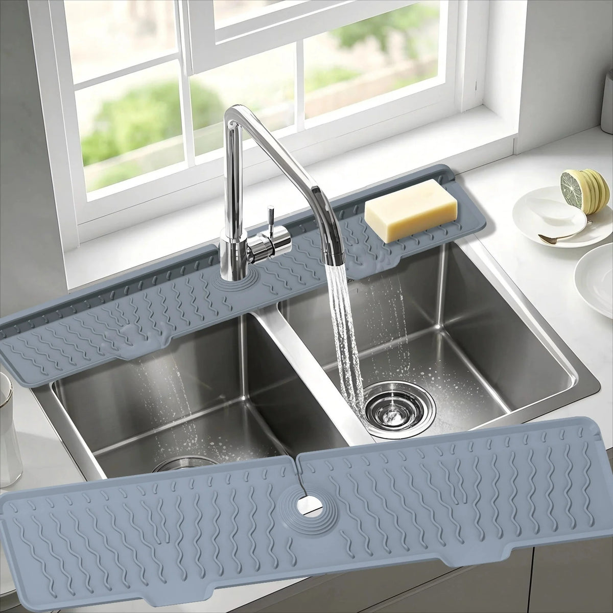 A silver faucet mat with a silicone design is placed in a kitchen sink under a window.