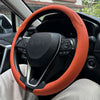Close-up view of a black steering wheel with an orange breathable leather cover installed in a car interior.