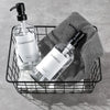 A black wire basket holds two clear glass bottles of premium conditioner and shampoo with stainless steel pumps resting on a 