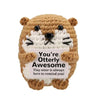 A handmade crochet animal doll resembling a bear with white fur and black features, holding a card that reads You're Otterly 