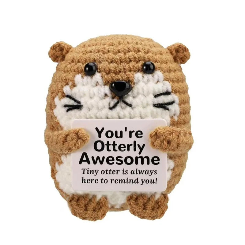 A handmade crochet animal doll resembling a bear with white fur and black features, holding a card that reads You're Otterly 